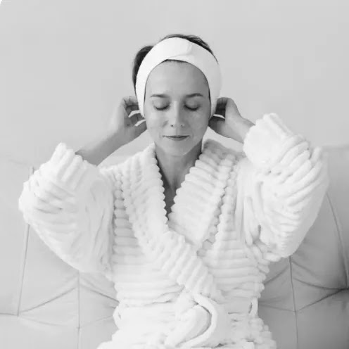 Woman in a plush white robe and headband relaxing, preparing for a soothing aesthetic treatment at PULSE Biohacking Med Spa in Winchester, VA.
